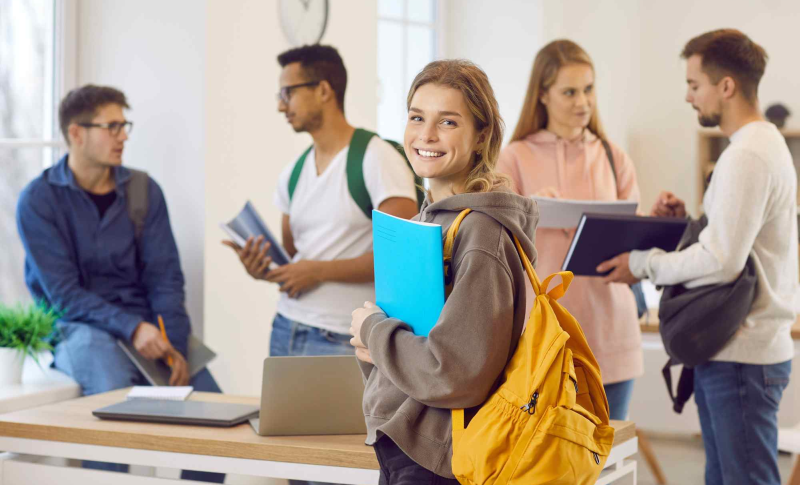 Gruppe junger Auszubildender mit Rucksäcken und Mappen in einem gemeinsamen Raum