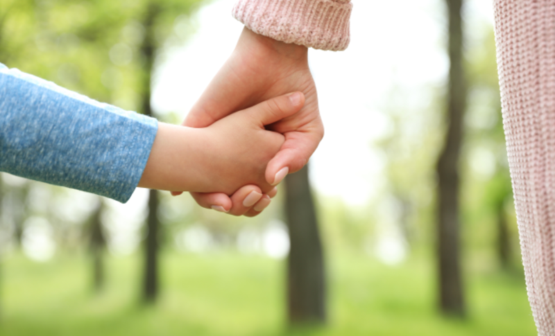 Eine kleinere Hand hält eine größere Hand im Freien