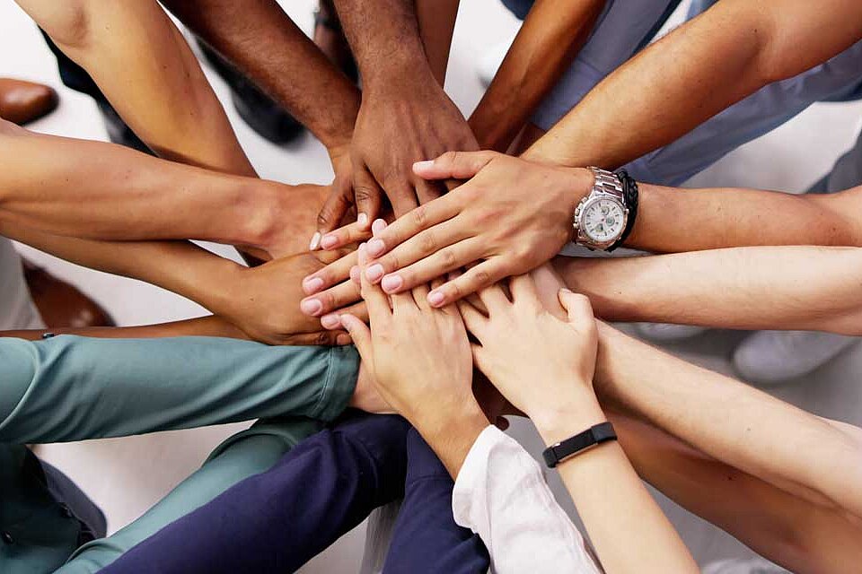 Hände mehrerer Personen liegen übereinander als Symbol für gemeinsames Arbeiten im Team