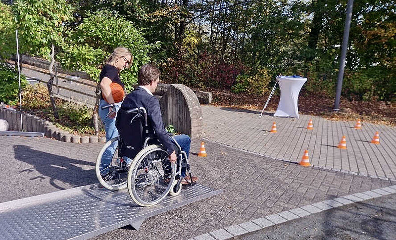 Eine Sozialarbeiterin begeleitet einen Mann im Rollstuhl auf einer Rampe.