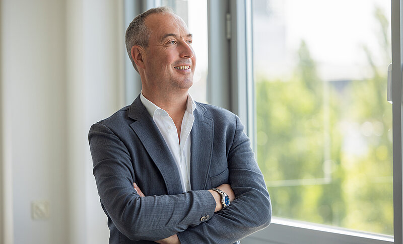 Geschäftsführer Volker Knöll blickt lächelnd und mit verschränkten Armen aus dem Fenster