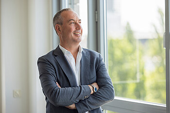 Geschäftsführer Volker Knöll blickt lächelnd und mit verschränkten Armen aus dem Fenster