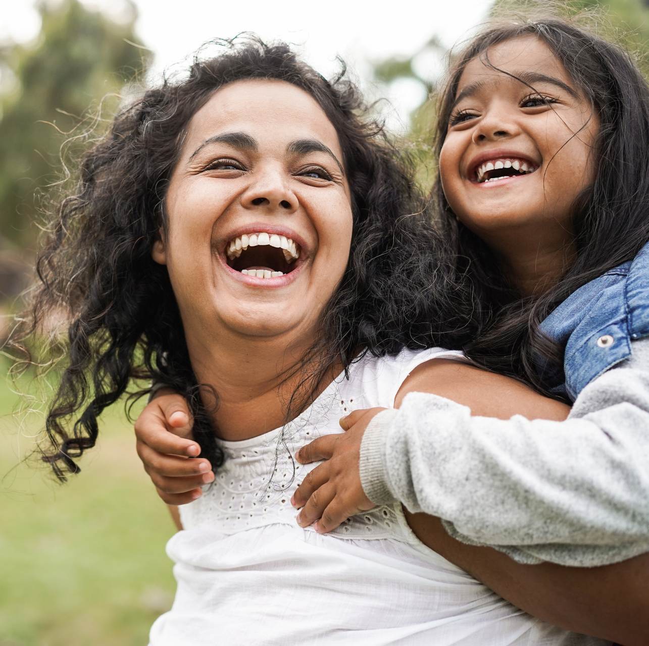 Eine lachende Mutter trägt ein lachendes Kind auf ihrem Rücken.