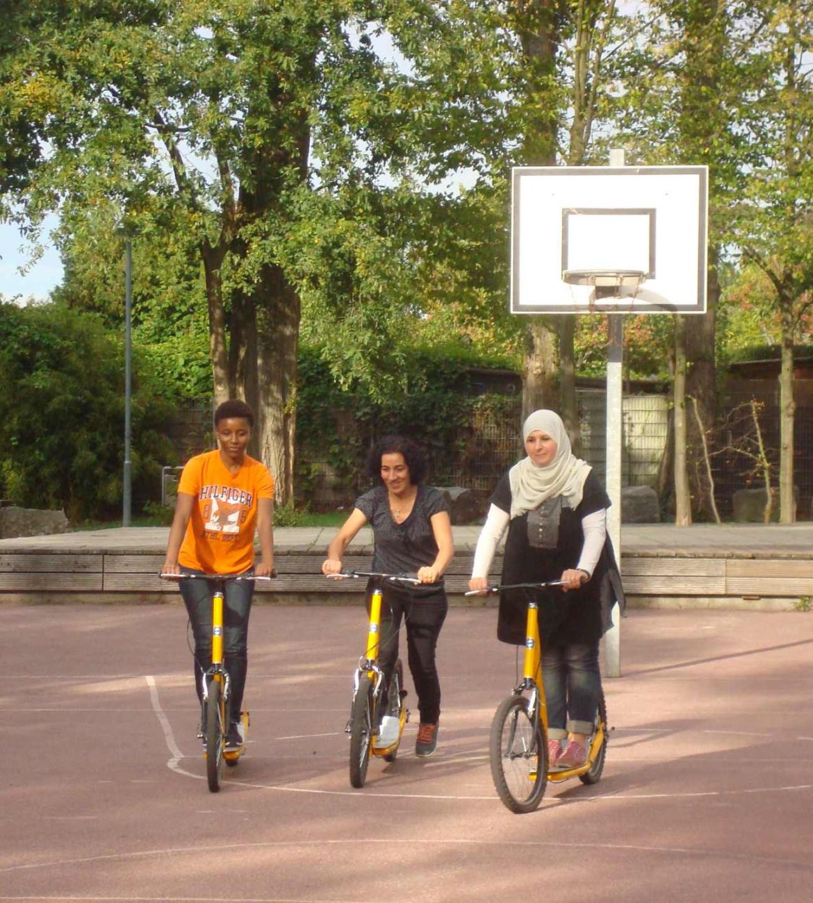 Vier Frauen üben mit dem Roller auf einem Sportplatz das Fahren.