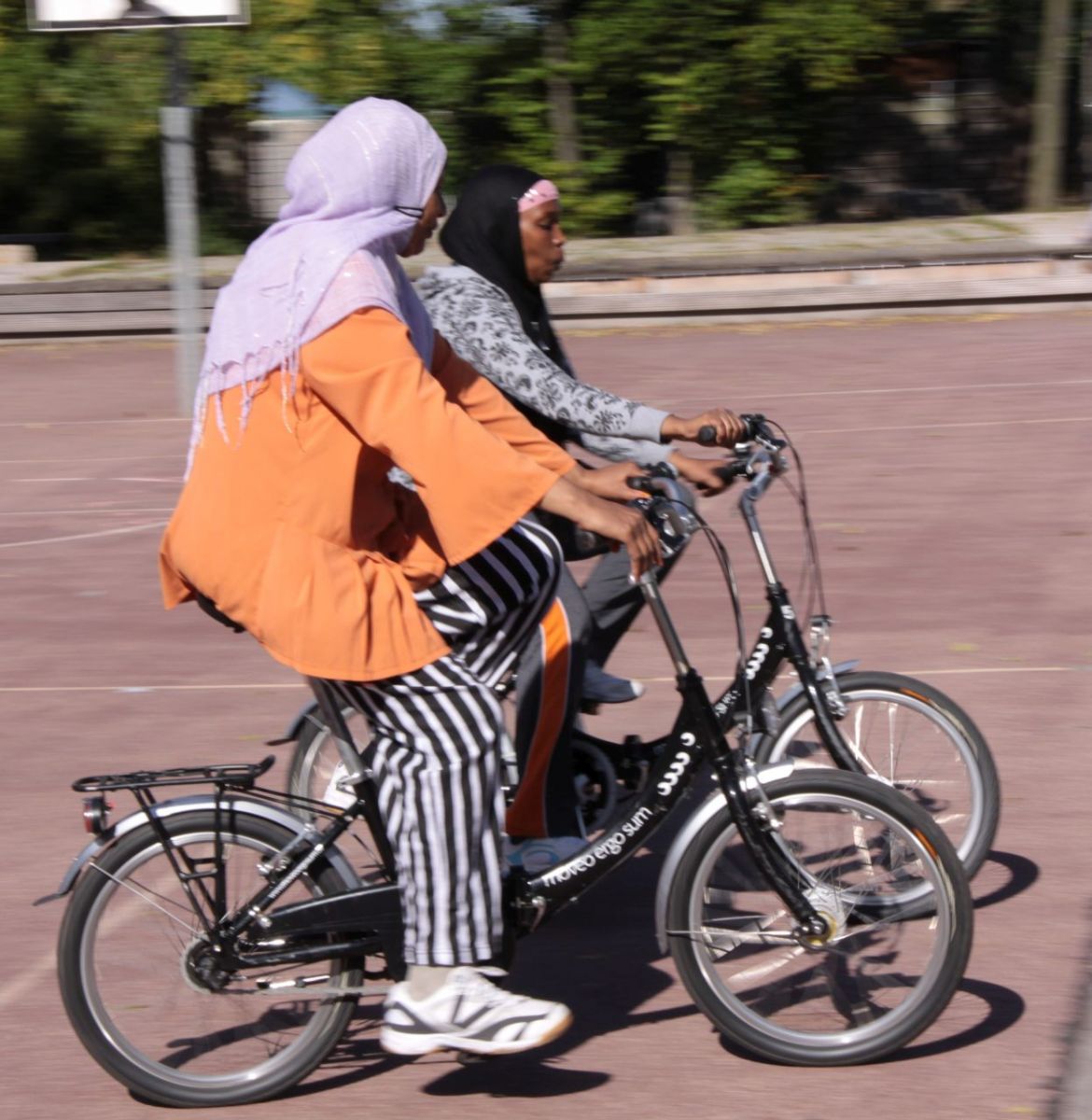 Zwei Frauen üben auf einem Sportplatz Fahrrad fahren.