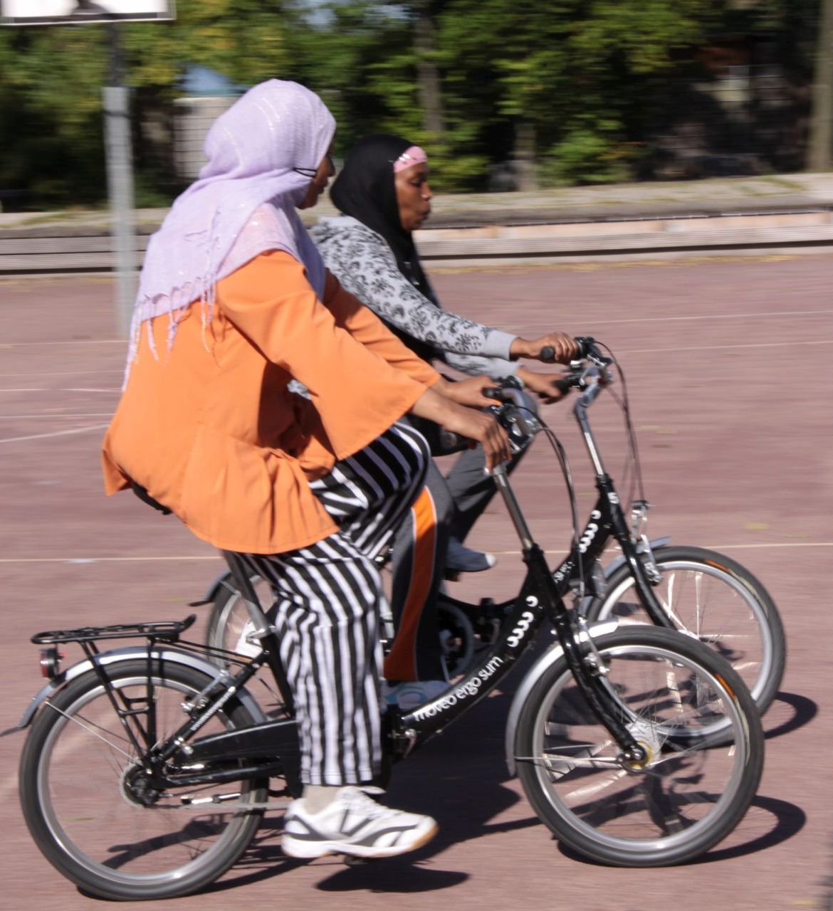 Zwei Frauen üben auf einem Sportplatz Fahrrad fahren.