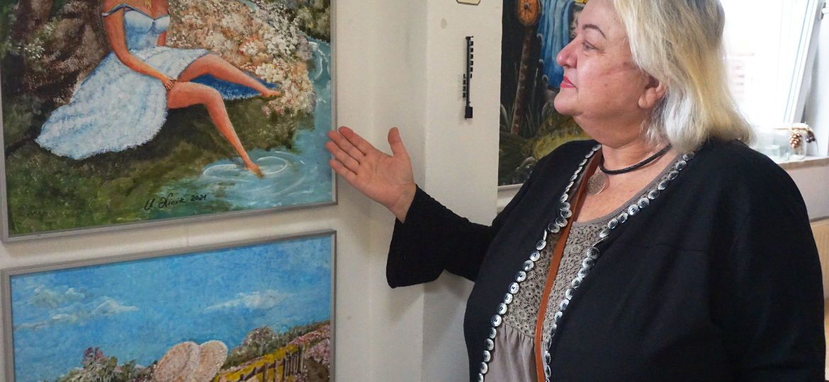 Künstlerin steht vor ihrem Werk, einem Gemälde einer Dame, die am Wasser sitzt